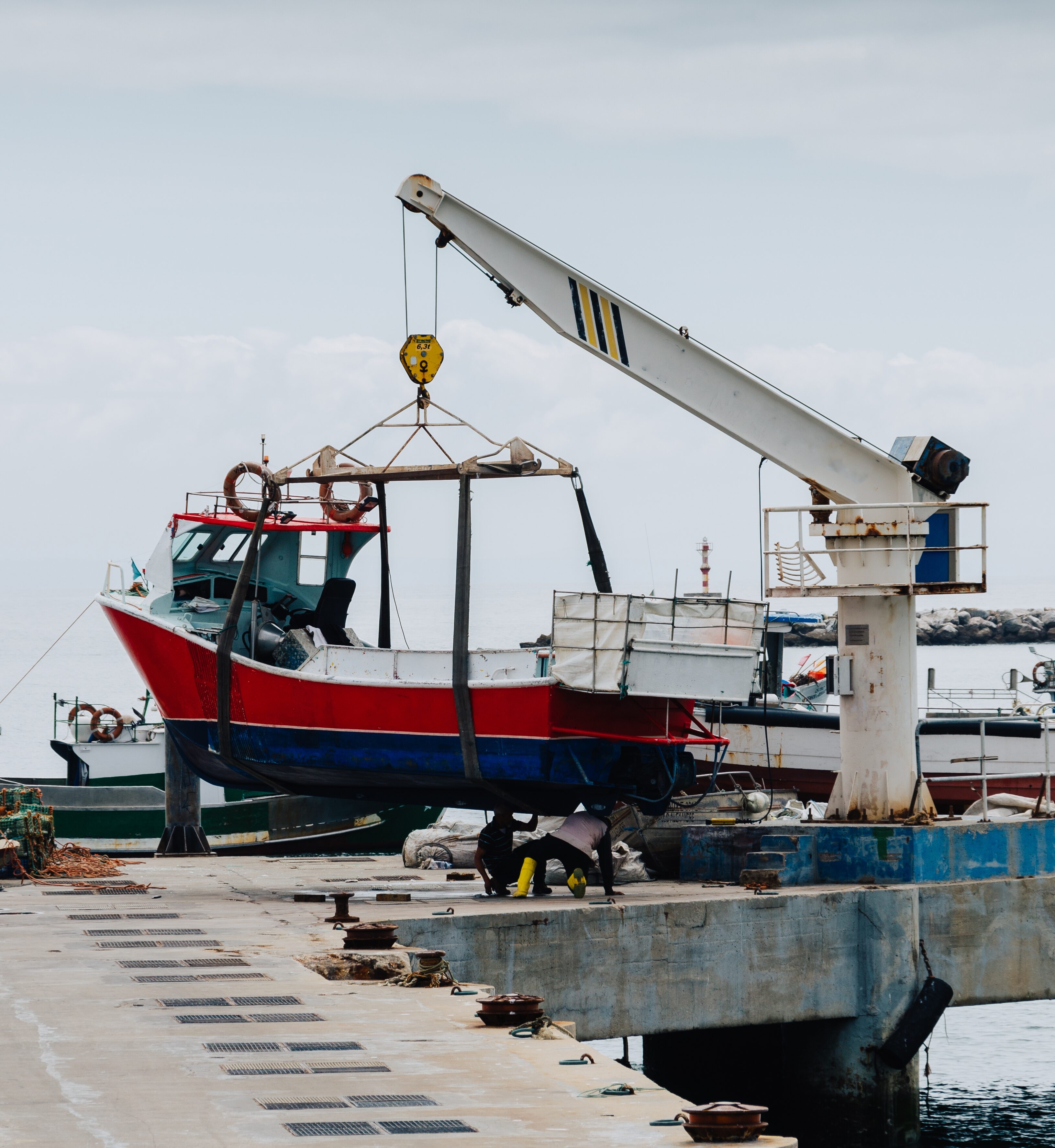 A vertical shot of a crane lifting a white boat on a pier